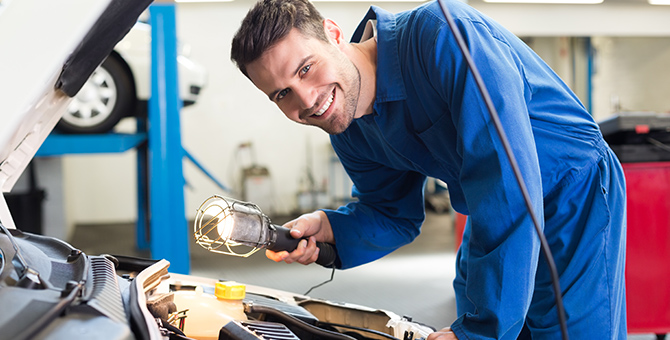 Smiling mechanic working on a car engine with a work light.